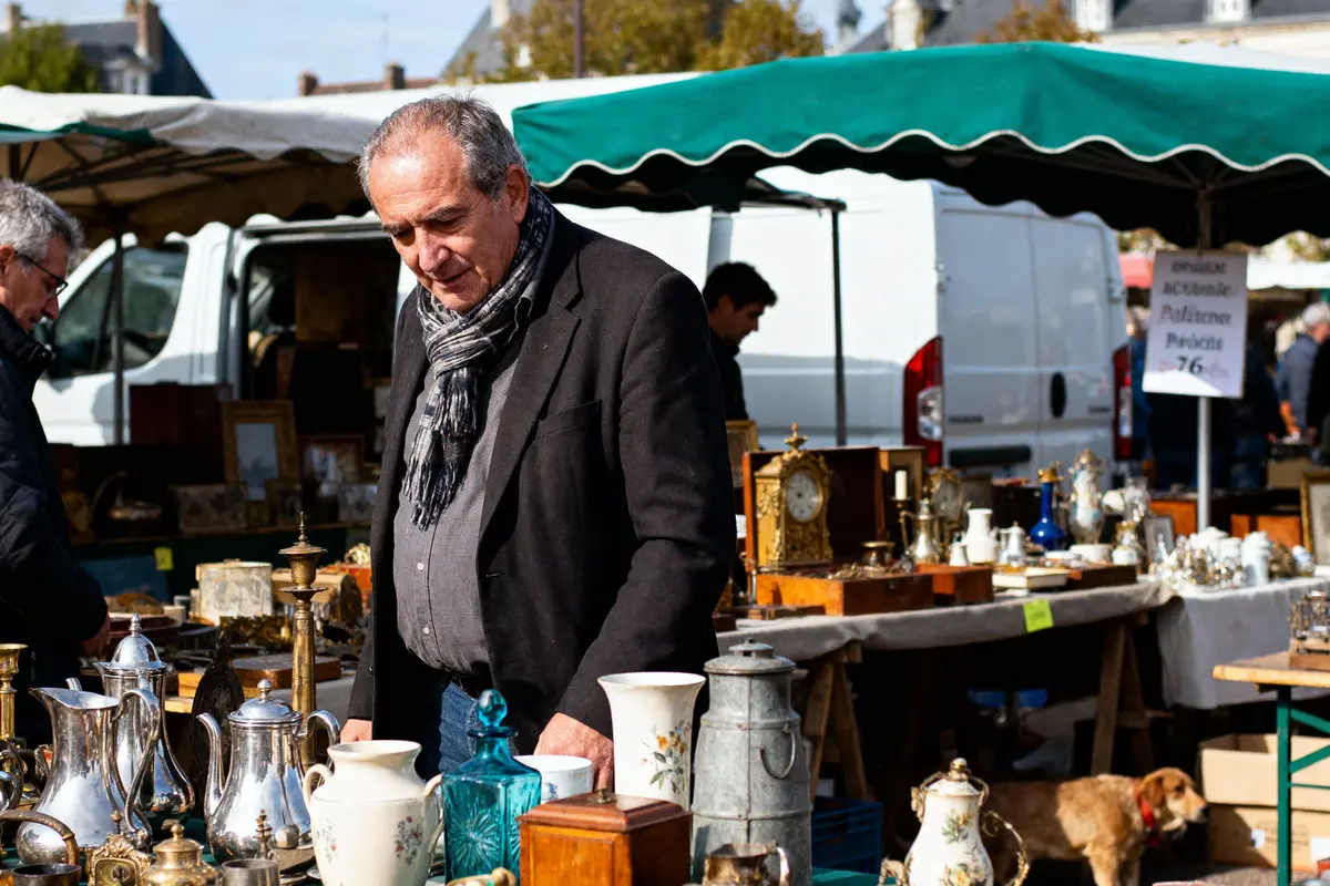 Homme regardant des antiquités sur un marché en plein air, avec divers objets anciens exposés sur les tables.