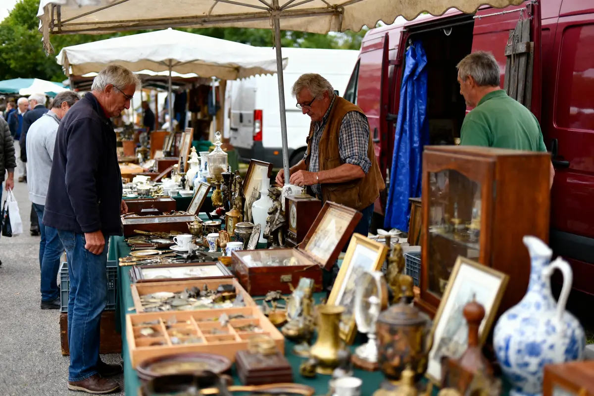 Marché aux puces animé avec objets anciens, hommes examinant des antiquités sous des parasols.