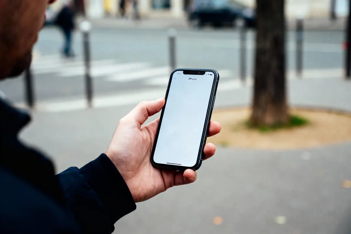 Personne tenant un smartphone avec écran vide dans une rue urbaine, en arrière-plan flou.