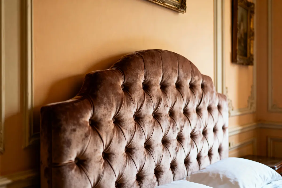Tête de lit capitonnée marron dans chambre classique, murs beiges, moulures et cadre doré.