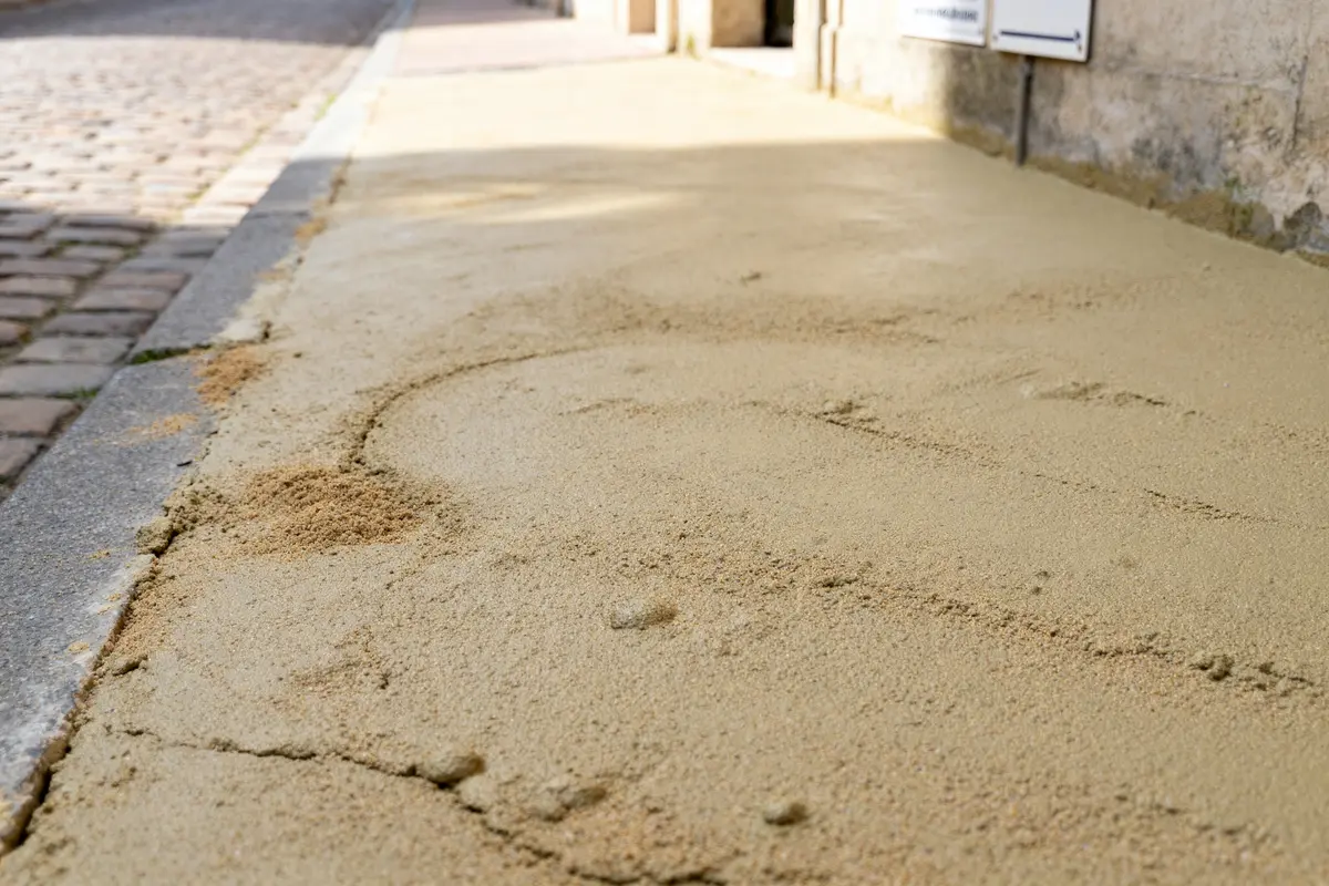 Chape maigre en ciment sur un trottoir près d'une rue pavée ensoleillée
