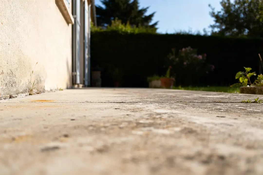 Vue en contre-plongée d'une dalle en béton longeant une maison dans un jardin verdoyant