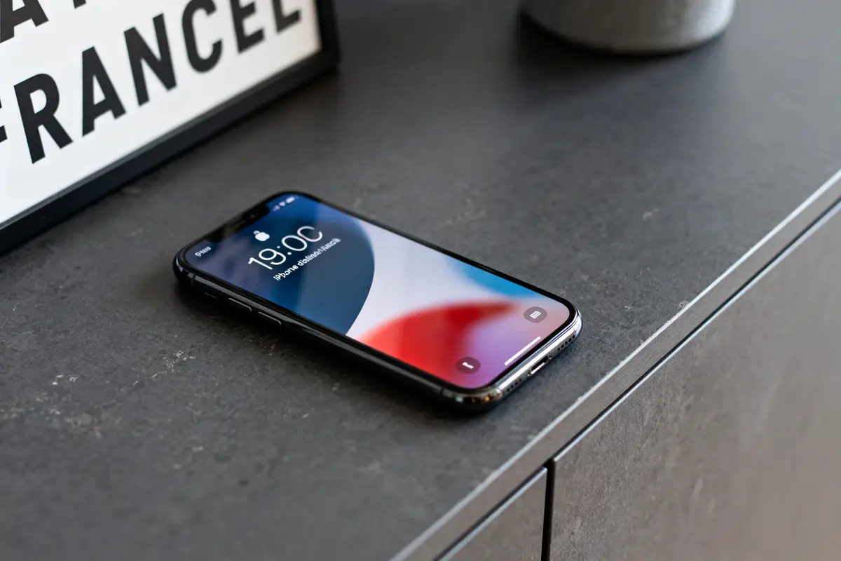 Smartphone posé sur une table sombre, affichant l'heure 19:00, à côté d'un tableau partiellement visible.