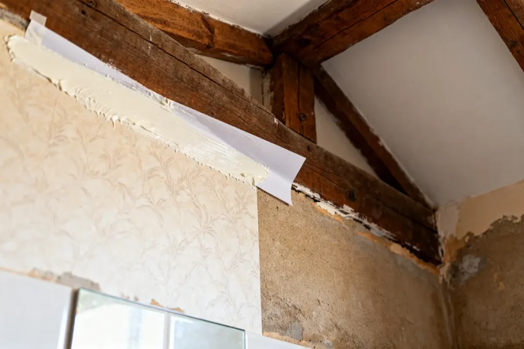Rénovation avec intisse papier peint appliqué sur mur sous poutres en bois apparentes