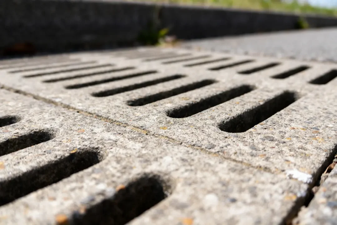 Gros plan sur une grille de drainage en béton avec ouvertures rectangulaires en extérieur.