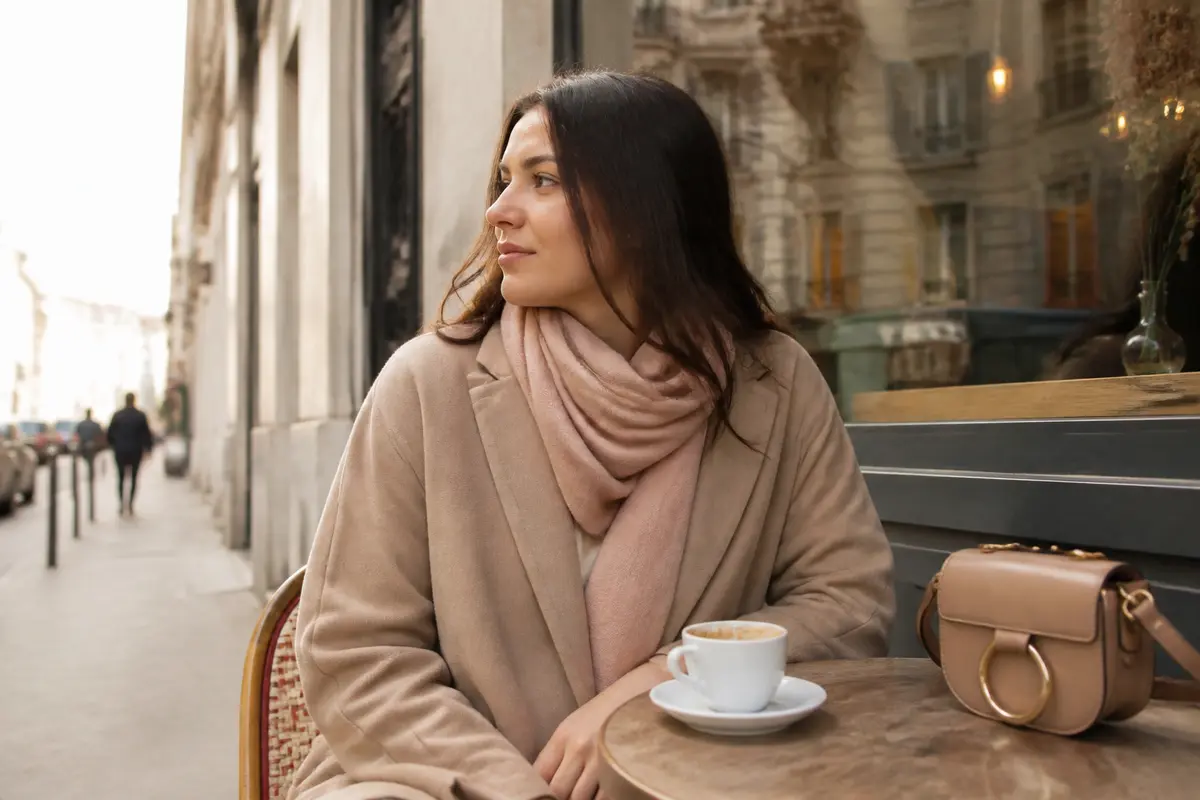 Femme en manteau couleur nude, café en terrasse avec sac assorti.